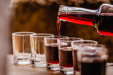 pouring red alcohol shots in small glasses on a celebration - obrazy, fototapety, plakaty