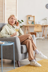 Mature woman sitting on armchair talking on mobile phone and drinking wine she has leisure time at home