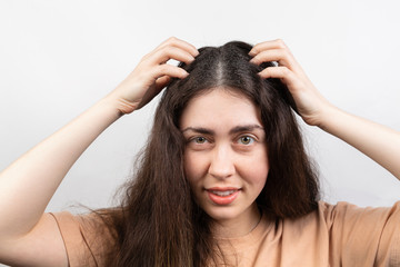Dandruff and lice. Portrait of a young Caucasian woman, a brunette, who scratches her head with her hands.White background