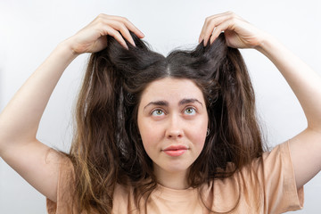 Fototapeta premium Dandruff, pediculosis and seborrhea. Portrait of a young Caucasian woman, a brunette, who lifts her hair with her hand, looking up. White background