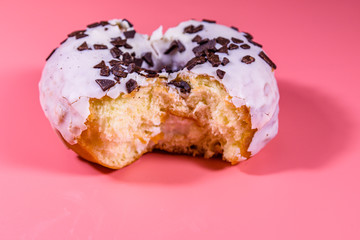 Bitten glazed donut with chocolate chip on top isolated on a pink background
