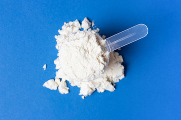 Scattered protein powder and scoop on blue background, top view