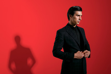 Obraz na płótnie Canvas Young handsome brunette man in elegant black suit over red background. Horizontal view with space for text.