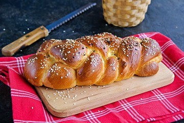 Homemade challah, traditional wicker white bread on a wooden board on a black concrete background. Copyspace