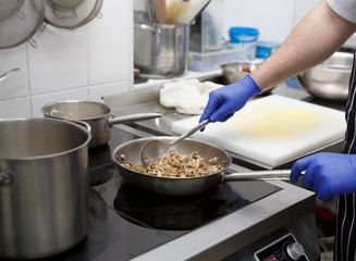 Man in gloves cooking mushrooms on frying pan