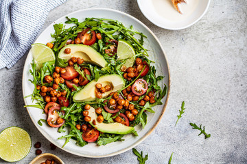 Roasted chickpea salad with avocado and tomatoes in white bowl, top view.  Healthy vegan food concept.