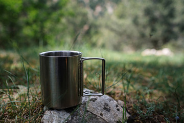 A mug with a hot drink stands on a stone in nature.