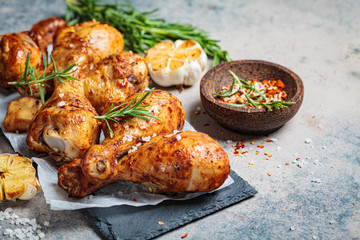 Baked spicy chicken legs with rosemary and garlic on black slate, dark background.