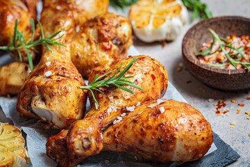 Baked spicy chicken legs with rosemary and garlic on black slate, dark background.