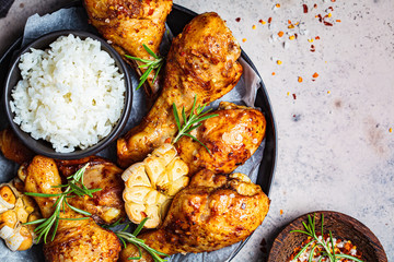 Baked spicy chicken legs with rice, garlic and herbs in black plate, dark background, top view.