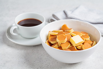 Pancake cereal with butter in a white bowl, tiny trend pancakes. Breakfast food concept.
