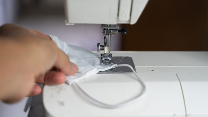 Electric sewing machine with fabric and thread, defocus hand hold on protective mask , antivirus  face mask during a pandemic virus COVID-19