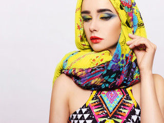 Portrait of a young woman with bright makeup and a fashionable headscarf. Light background. Beauty, fashion, makeup concept.