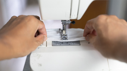 Electric sewing machine with fabric and thread, defocus hand hold on protective mask , antivirus  face mask during a pandemic virus COVID-19