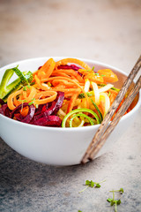 Vegetable noodles - zucchini, beets and carrots in white bowl, dark background. Raw vegan food.
