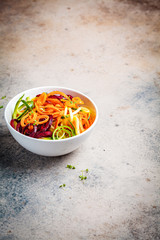 Vegetable noodles - zucchini, beets and carrots in white bowl, dark background. Raw vegan food.