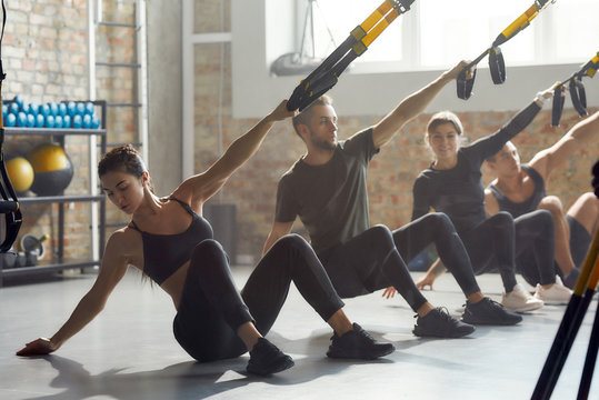 Fitness Together. Full-length shot of men and women doing fitness TRX training exercises at industrial gym. Push-up, group workout concept