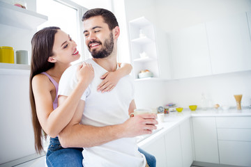Photo of two people man woman hug embrace piggyback have rest relax weekend man hold mug beverage coffee latte girl sit window sill in kitchen house indoors