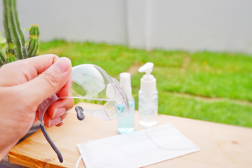 Hand holding protective glasses with alcohol gel background.Men's hand holds protective medical glasses. Protective medical masks on background. Protection from pollution, virus, from COVID19.Close up