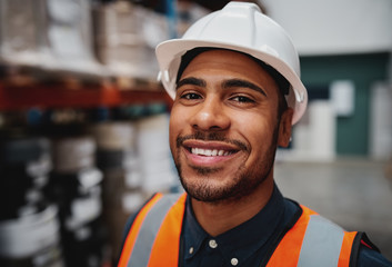 Portrait of smiling warehouse supervisor wearing white helmet hard hat smiling at the camera 