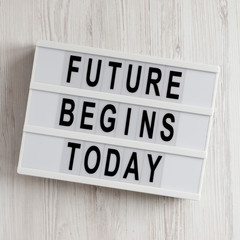 'Future begins today' words on a lightbox on a white wooden background, top view. Overhead, from above, flat lay.