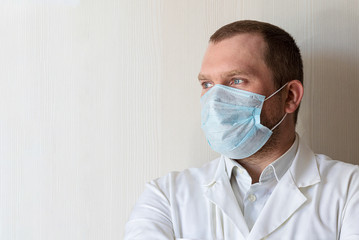 A serious young male doctor in a medical mask with a gaze. Health