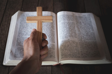 The crucifix in human hands rests on the Bible. Concepts for the study of Christians, Christianity, Catholicism, God, Heaven, Heaven, God or God. God helps to repent, pray for Easter, Catholic Lent.