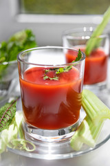 Two glasses of tomato juice with parsley and celery decorations, stand near the window, morning sunlight shines, shallow depth of field, selective focus. Natural drinks concept.