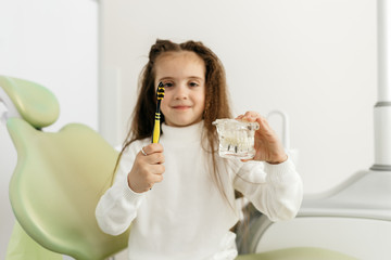 Girl in dentist's office shows how to brushing your teeth