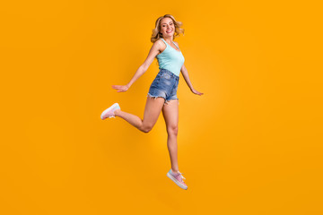 Fototapeta na wymiar Full size profile photo of attractive pretty lady good mood jump high up excited expression walking down street wear teal tank-top denim shorts shoes isolated yellow color background