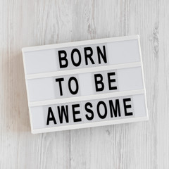 'Born to be awesome' words on a lightbox on a white wooden background, top view. Overhead, from above, flat lay.
