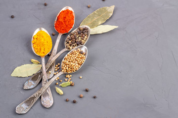 Dry spices of different colors in teaspoons and bay leaf. Top view