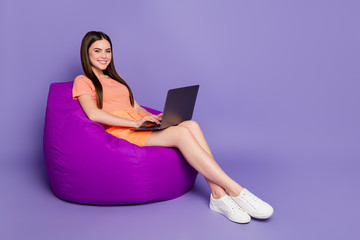 Full size profile photo of cheerful lady sitting comfy beanbag browsing notebook freelance work wear orange striped t-shirt jeans mini skirt isolated pastel purple color background