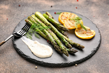 Cooked asparagus with sauce and lemon on grey background