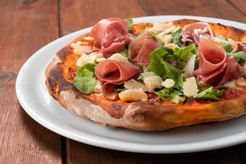 Deliziosa pizza emiliana con fette di prosciutto crudo, parmigiano e insalata 