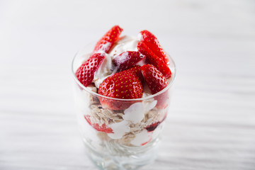 Strawberry dessert in a plate with ice cream and cream on a white wooden background
