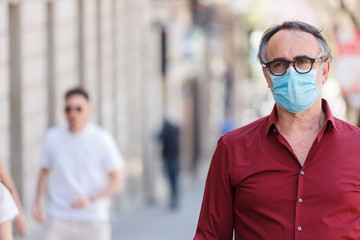 Uomo con mascherina vestito casual cammina per la città protetto dalla mascherina chirurgica