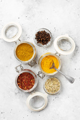 Spices and condiments in glass jars on a light gray table. Spices close-up with space for text. The view from the top