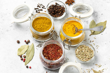 Spices and condiments in glass jars on a light gray table. Spices: turmeric, curry, star anise, fennel and cloves close-up with space for text