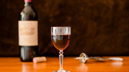 A GLASS OF WINE WITH SEVERAL BOTTLES OF WINE IN THE BACKGROUND 