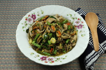 Fried spicy fresh mussel meats with chilly, cutting green bean, chopped fresh baby corn and basil on the plate. Famous comfortable seafood menu in Asia. Hot plate in street food. 