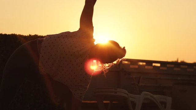 Smooth traveling of how the sun appears behind a young woman while doing yoga pose at sunrise with a strong sun backlight.