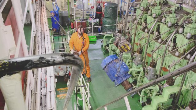 skilled engineer in orange costume operates professional crane with blue tanker winch electric motor detail