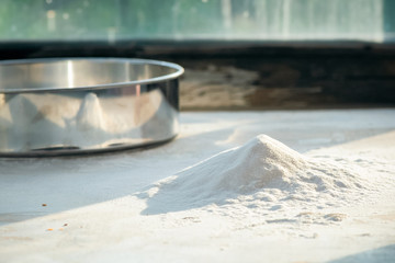 A sieve and flour on the rustic kitchen table close up.