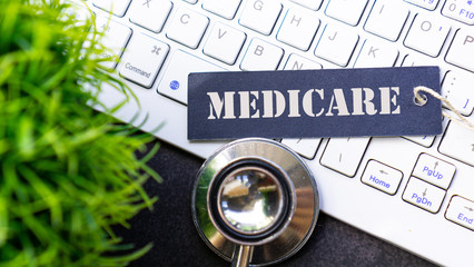 MEDICARE text on a label with white keyboard, stethoscope, and green grass background medical concept