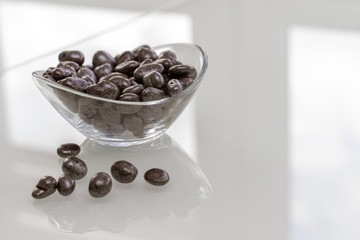 raisins in chocolate in a glass bowl on a glossy light surface