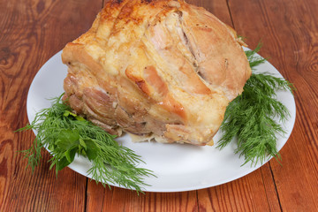 Piece of baked pork on the white dish with greens