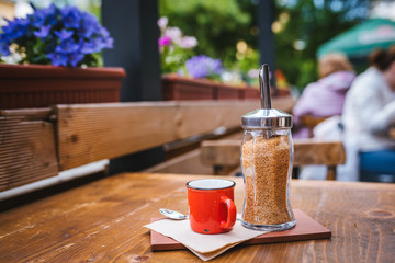 Outdoor cafe table with an espresso in a mug on the table and flower decoration on the background.