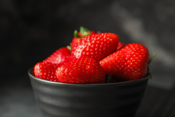 Bowl with ripe strawberry on dark background