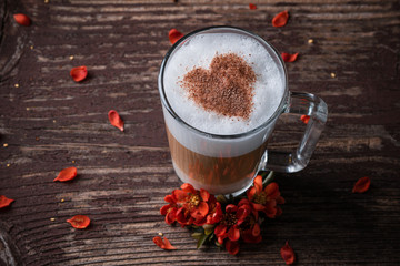 A glass with latte macchiato on wooden background with red flowers